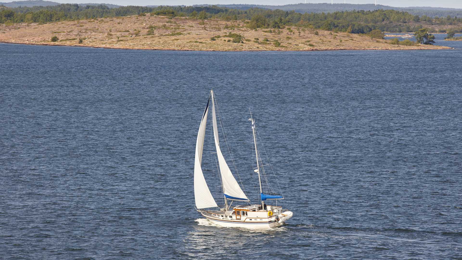 Ein Segelboot gleitet durch die blauen Gewässer des Åland-Archipels, mit einer ruhigen Insel im Hintergrund.