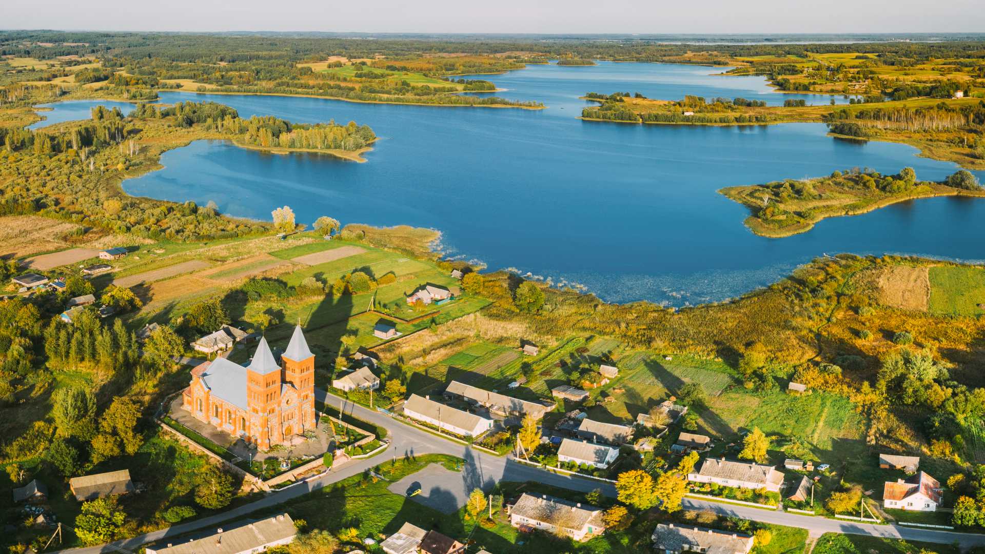 Aerial view of Ikazn village with its church, lush greenery, and serene lakes in Vitebsk Voblast, Belarus.