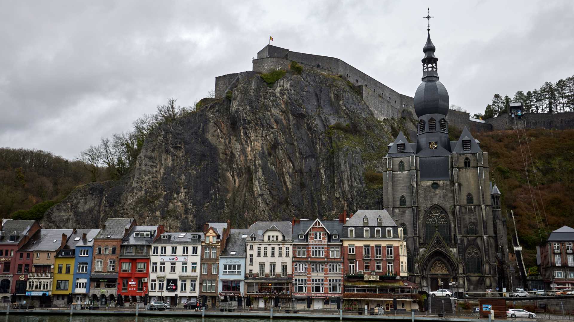 Kleurrijke huizen staan langs de rivier, met de gotische collegiale kerk en de Citadel van Dinant bovenop een rotsachtige heuvel.