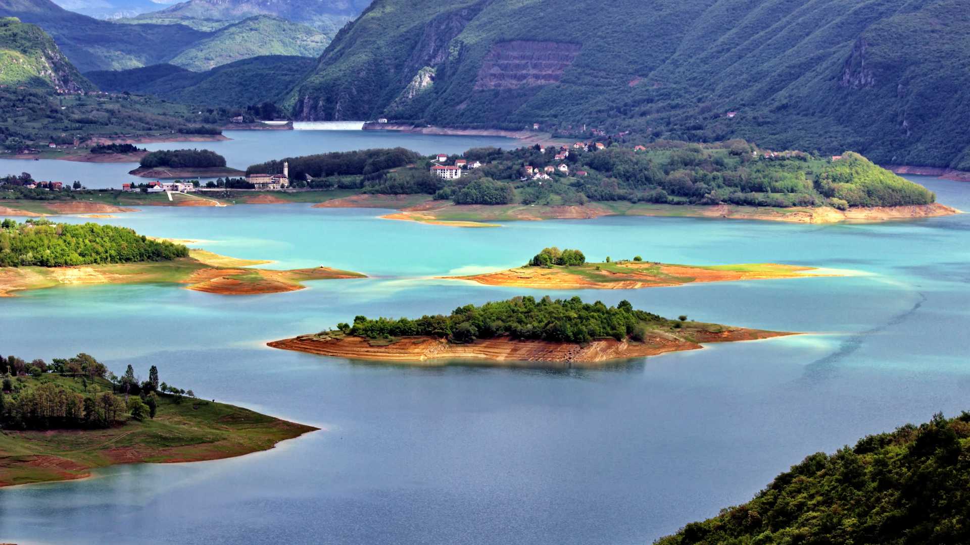 Lush green islands dot the turquoise waters of Lake Varvara, framed by forested hills in Bosnia and Herzegovina.