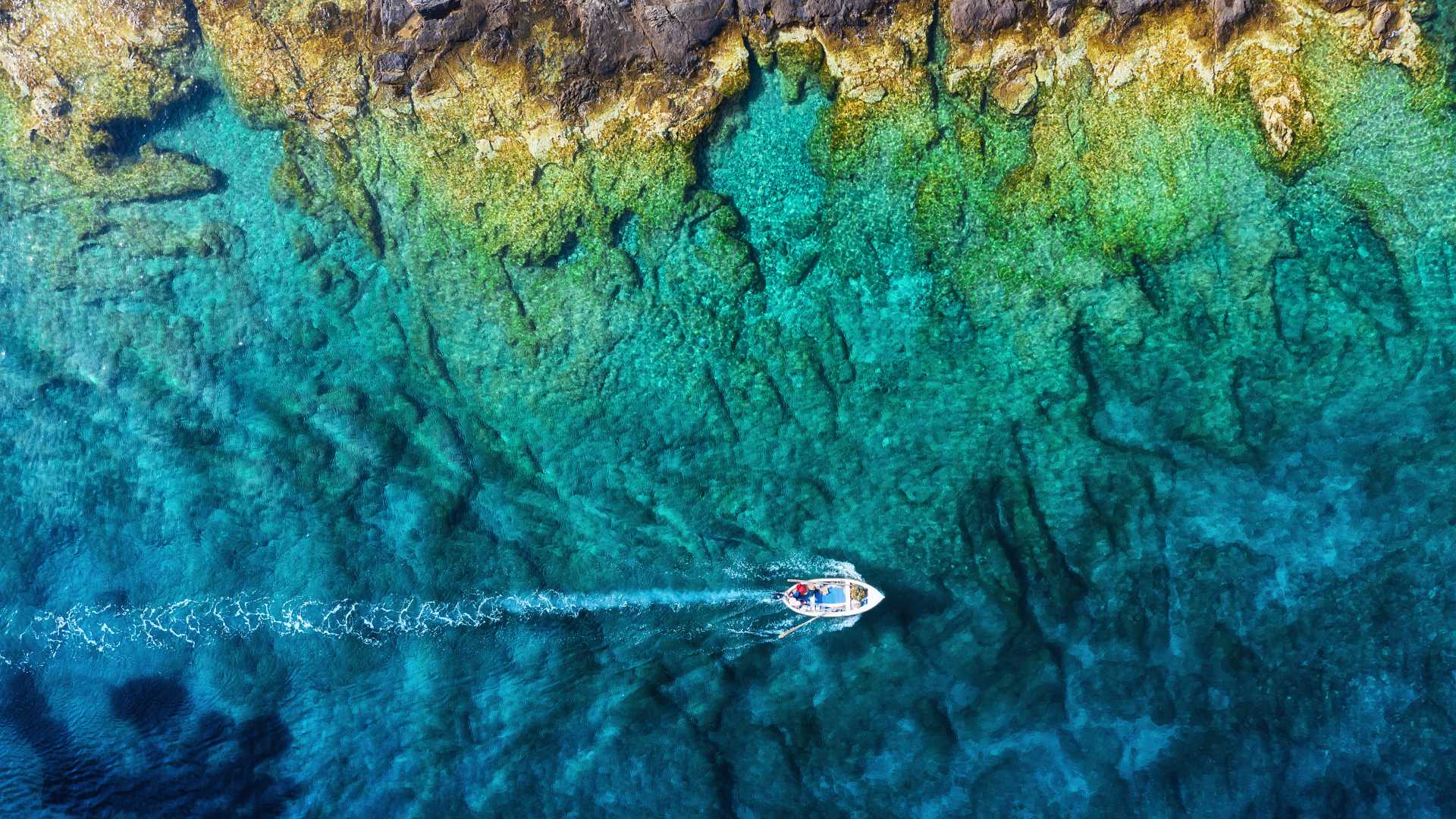 Luftaufnahme eines Bootes, das über das klare, türkisfarbene Wasser der Adria in der Nähe der Küste Kroatiens gleitet.