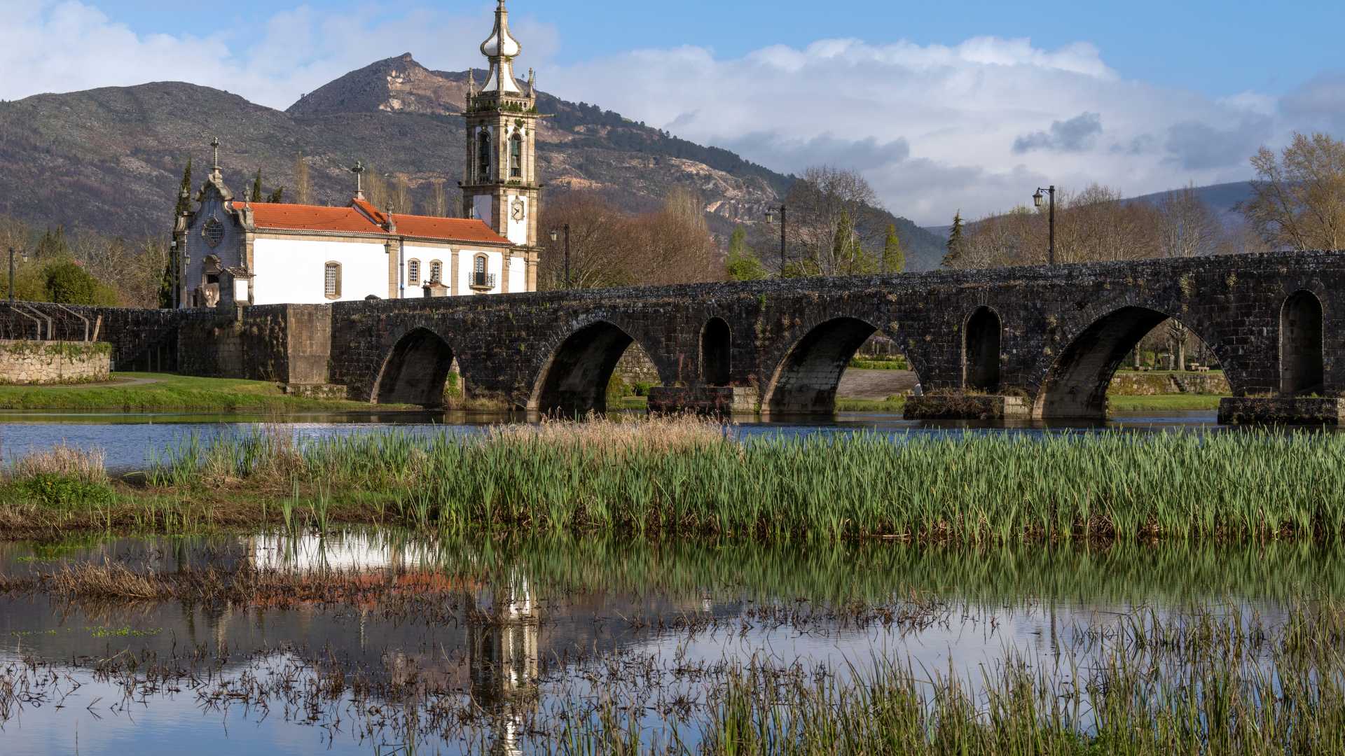 Middeleeuwse stenen brug over de rivier de Limia met een witte kerk en bergen op de achtergrond in Ponte de Lima, Portugal.