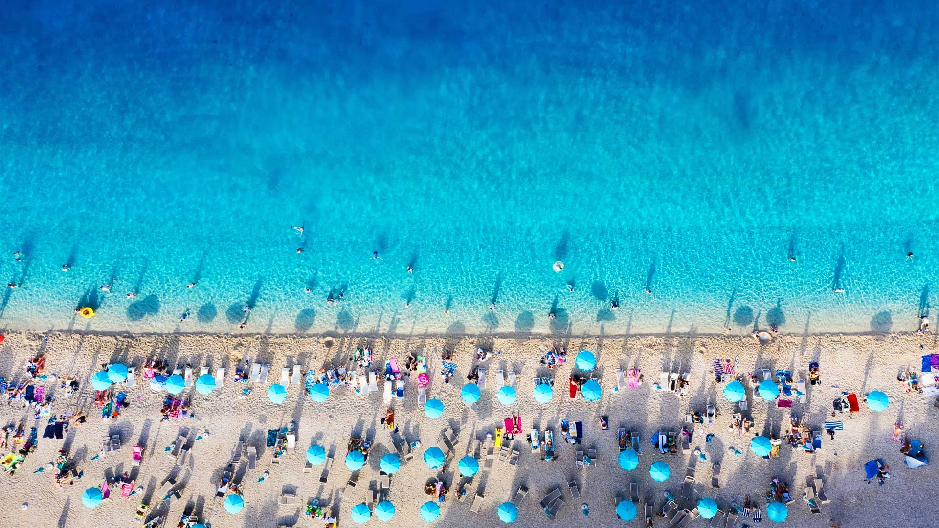 Luftaufnahme des Strandes Zlatni Rat, Kroatien. Azurblaues Wasser trifft auf ein sonnenbeschienenes Ufer mit blauen Sonnenschirmen.