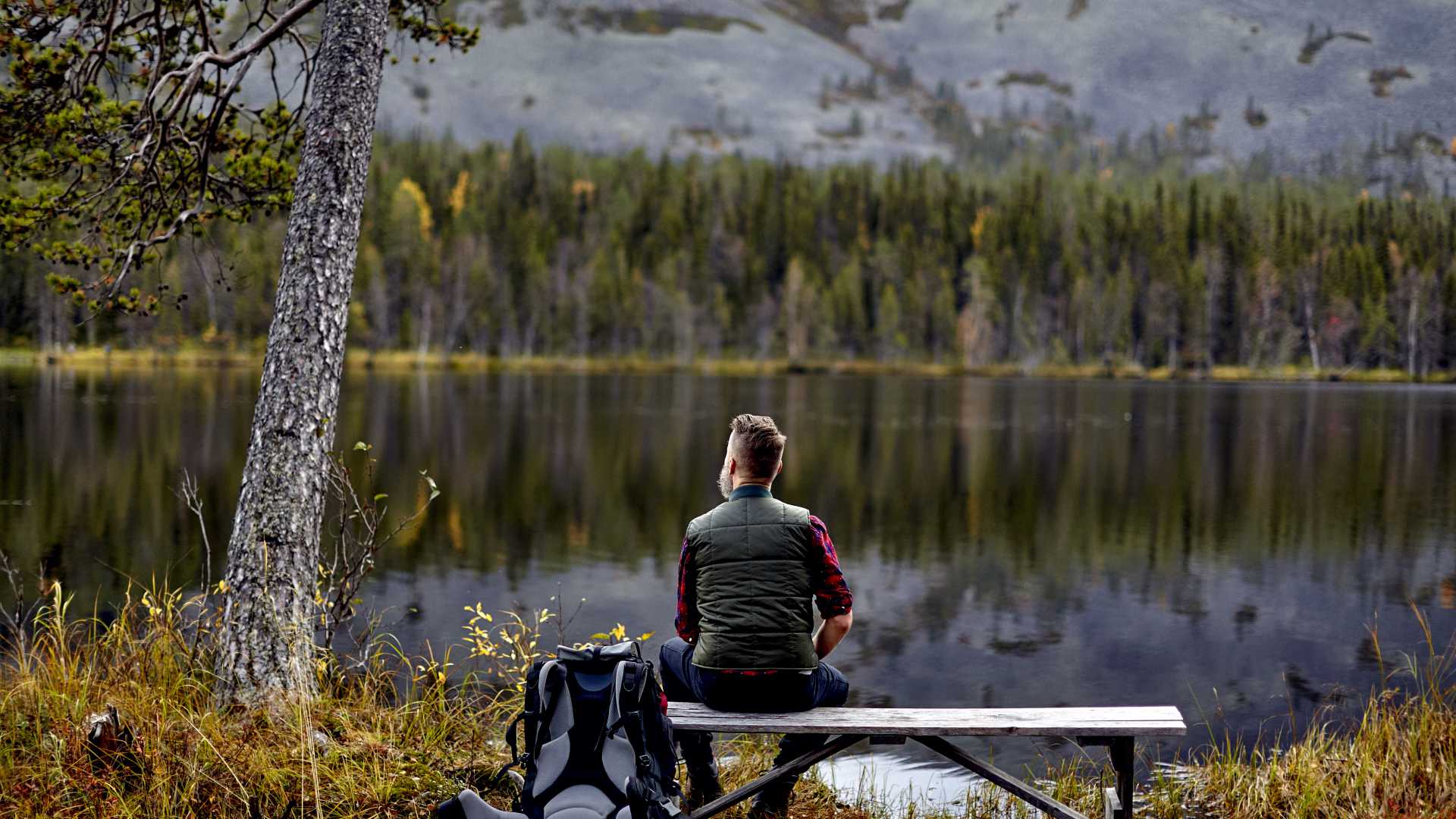 Een wandelaar rust uit op een bankje, starend naar het serene Kesankijarvi meer in Lapland, Finland, omringd door herfstbladeren.