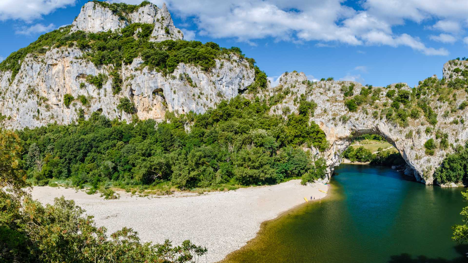 Vista dell'arco naturale di pietra calcarea Pont D'arc nel canyon dell'Ardeche con persone che praticano attività all'aperto come canoa e campeggio