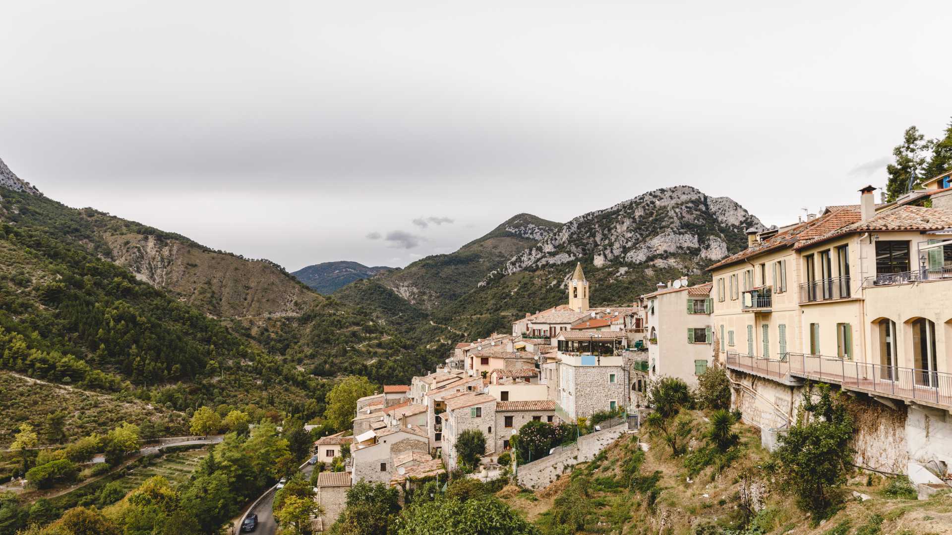 Charmant village de Sainte-Agnès, en France, niché au milieu de montagnes luxuriantes et escarpées, sous un ciel nuageux.