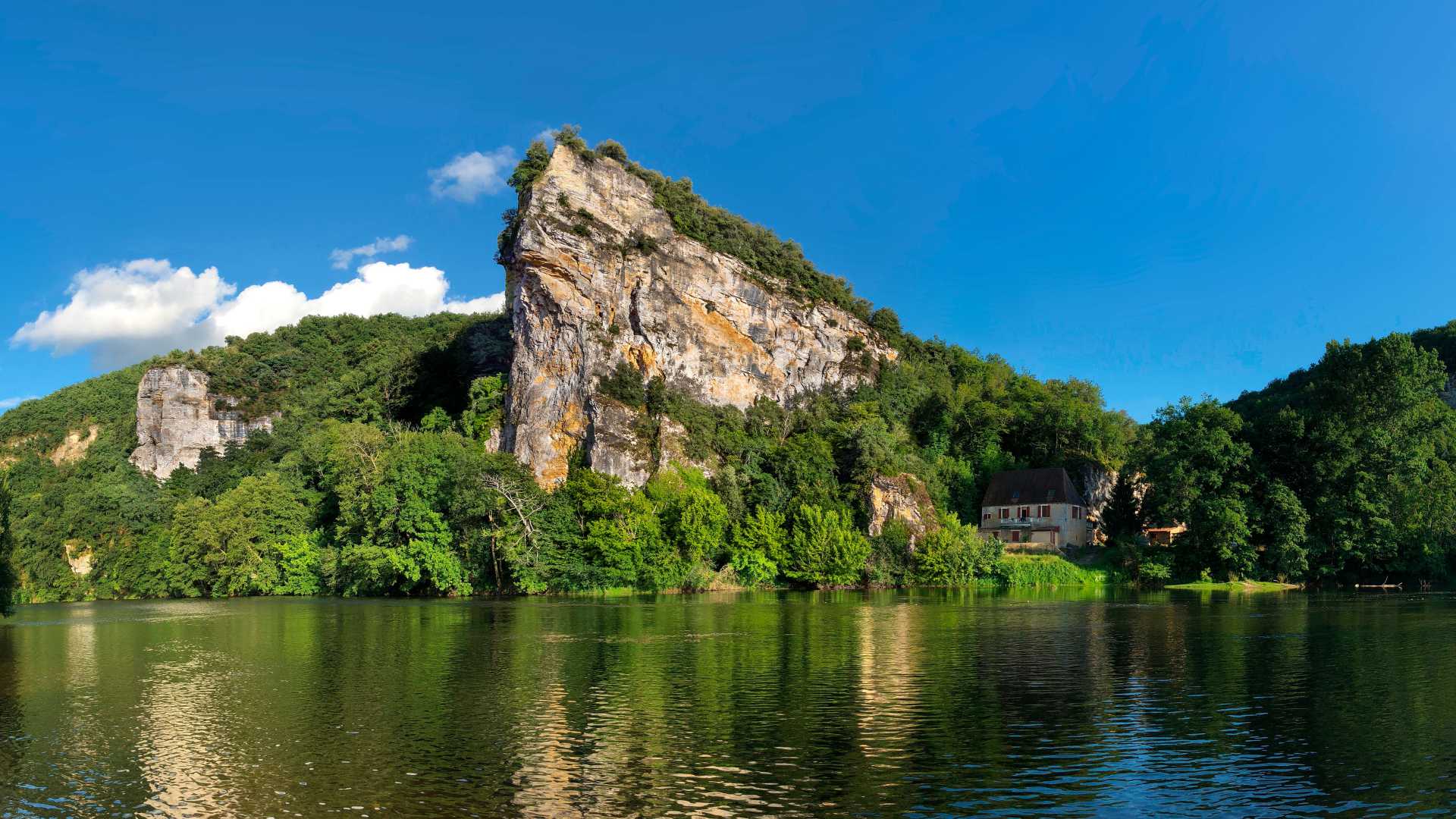 Späte Nachmittagssonne auf der Dordogne, mit Klippen und üppigem Grün, das sich im ruhigen Wasser spiegelt.