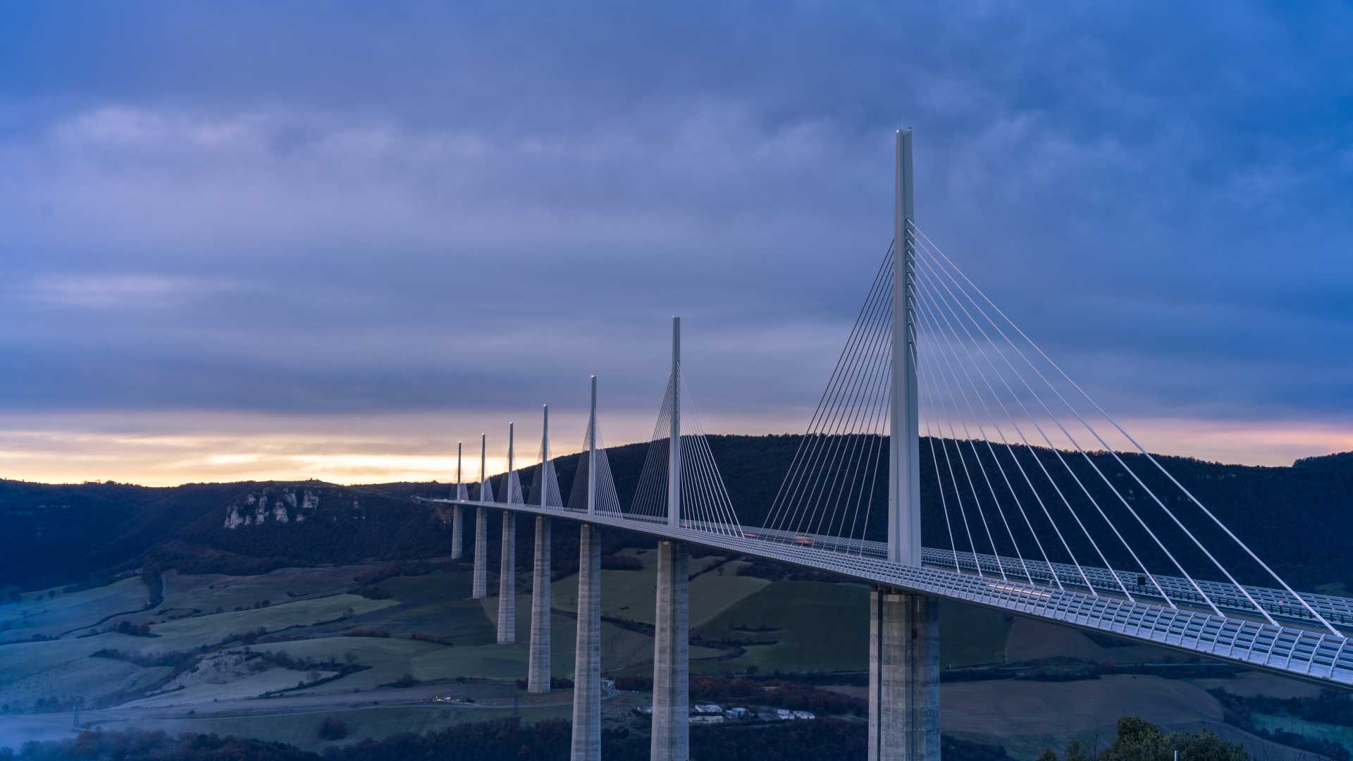 The Millau Viaduct towers over a misty valley at dawn, its sleek design cutting through the serene landscape.