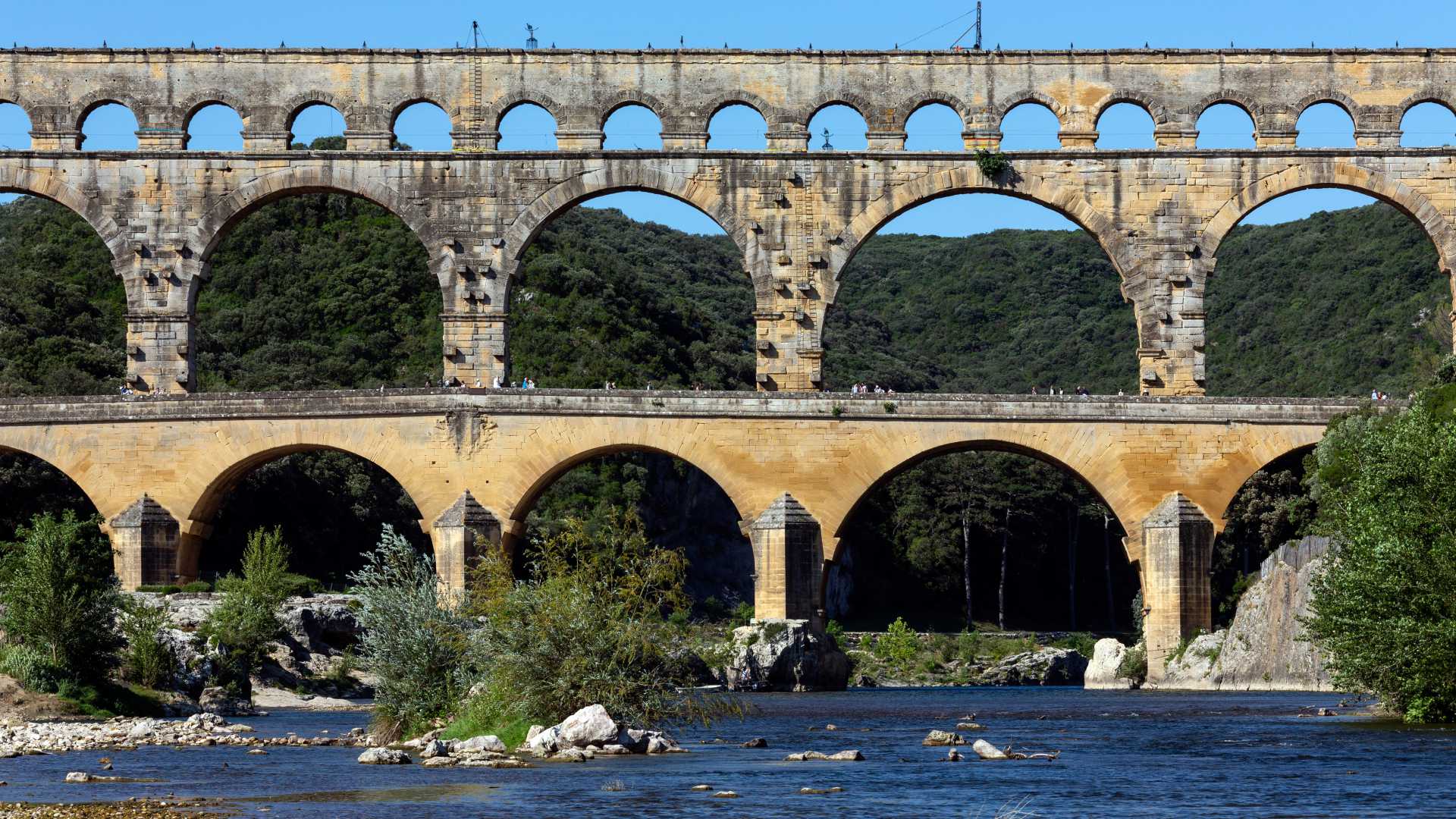 The impressive Pont du Gard, a Roman aqueduct, spans the Gardon River amidst green landscape.