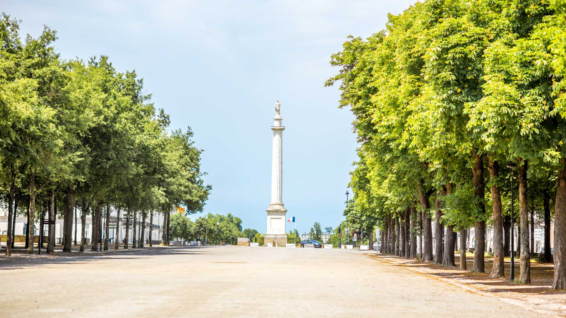 Allée bordée d'arbres menant à la colonne Louis dans le parc Saint-Pierre, à Nantes, par une matinée lumineuse.