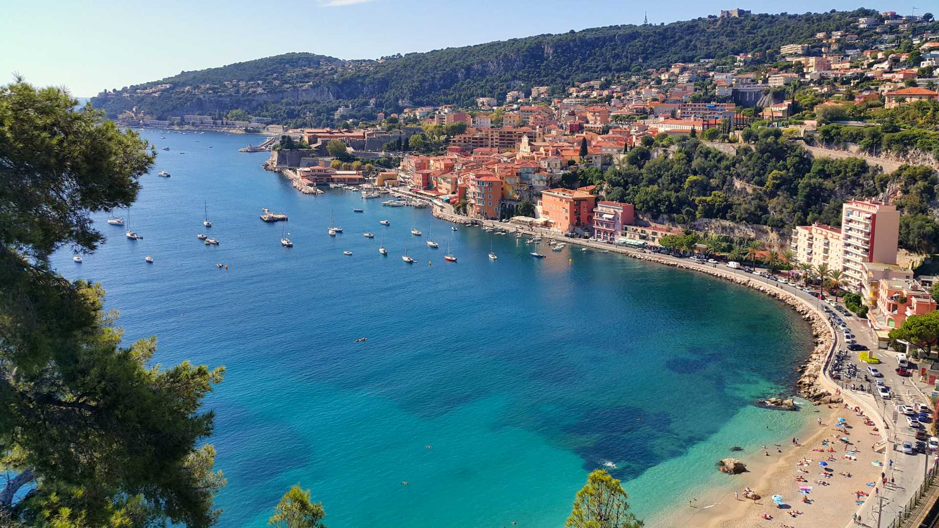 Kleurrijke gebouwen omzomen de serene haven van Villefranche-sur-Mer, met turquoise water en weelderige heuvels.