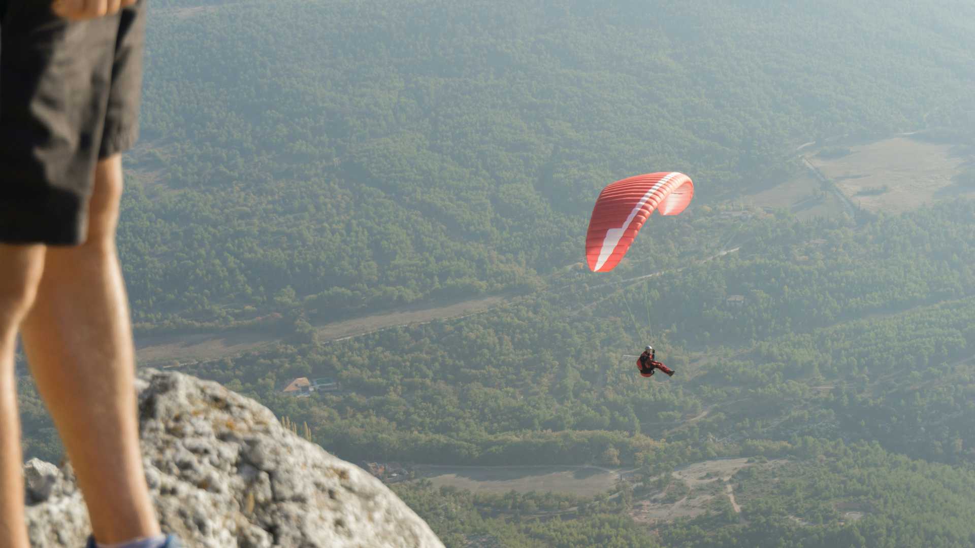 A paraglider with a red canopy enjoys panoramic views over a lush, green landscape in Provence.