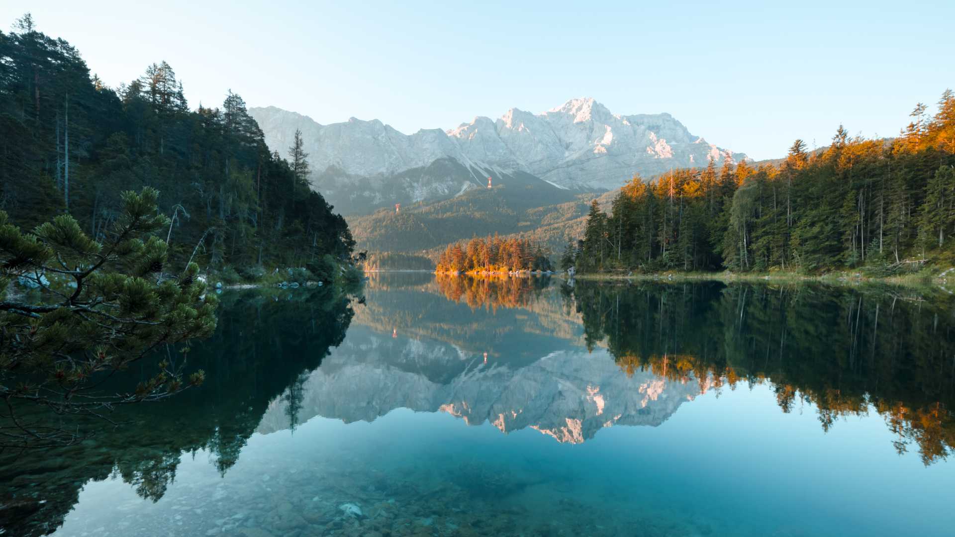 Das Morgenlicht beleuchtet den Eibsee mit den Spiegelungen der Alpen und des umliegenden Waldes. Bayerische Beschaulichkeit.