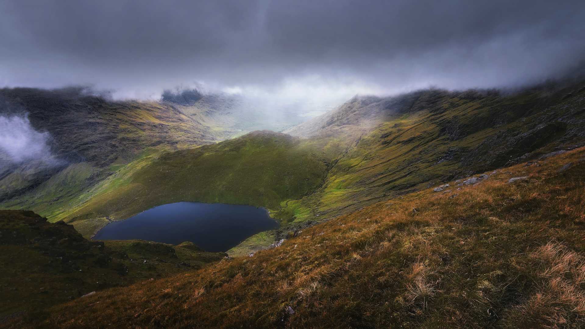 Sombere luchten boven Carrauntoohil, met een sereen meer genesteld tussen de weelderige groene heuvels van Iveragh Peninsula.