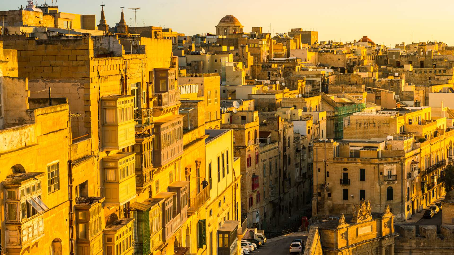 Golden sunrise over Valletta's historic rooftops and facades, bathed in warm morning light.