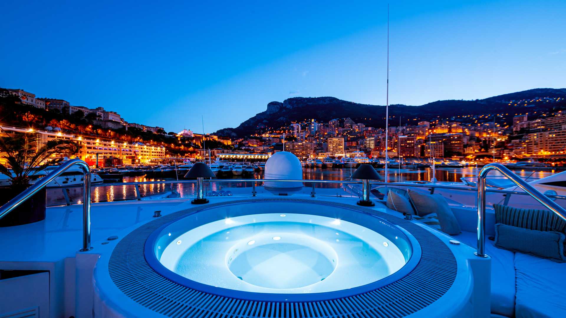 Vista nocturna de la piscina de un yate con arquitectura urbana iluminada al fondo