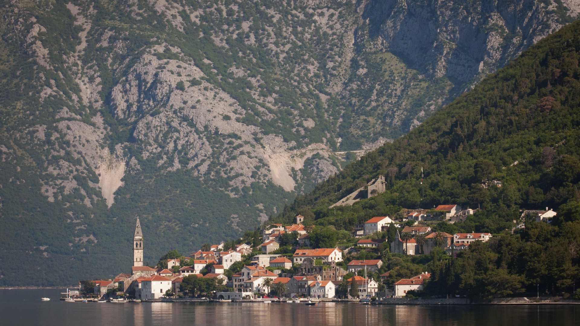 Charmantes Dorf mit roten Dächern an einem Berghang, der sich in einem ruhigen See in Montenegro spiegelt.