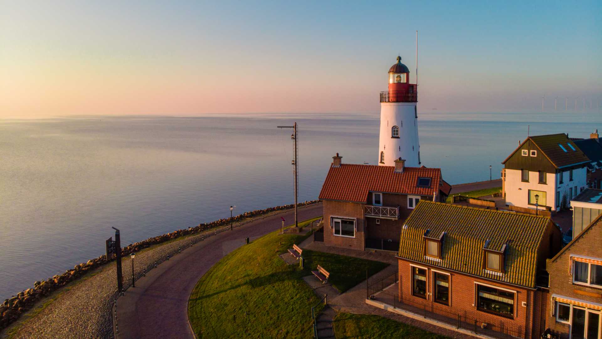 Leuchtturm und Hafen von Urk bei Sonnenuntergang, mit ruhigem Wasser und traditionellen niederländischen Häusern, Niederlande.