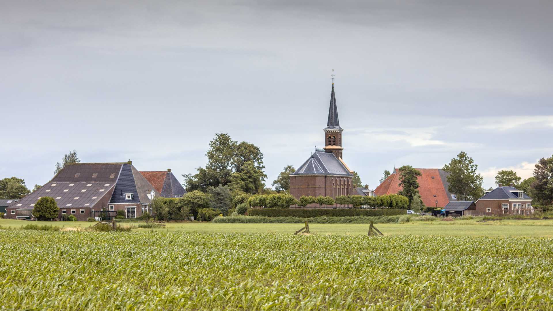 Charming Dutch hamlet of Warstiens, featuring a quaint church and traditional farm barns in lush Friesland.