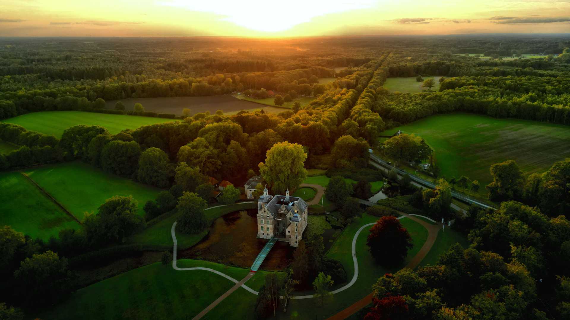 Luftaufnahme des in einen goldenen Sonnenuntergang getauchten Schlosses Ruurlo, umgeben von üppigem Grün in Gelderland, Niederlande.