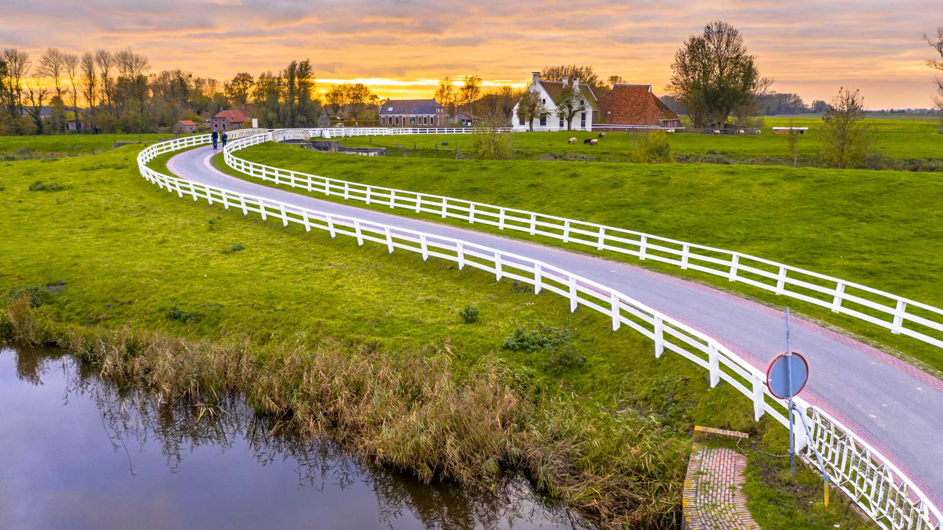 Paesaggio della campagna olandese con case storiche lungo una strada curva con una recinzione bianca durante il tramonto