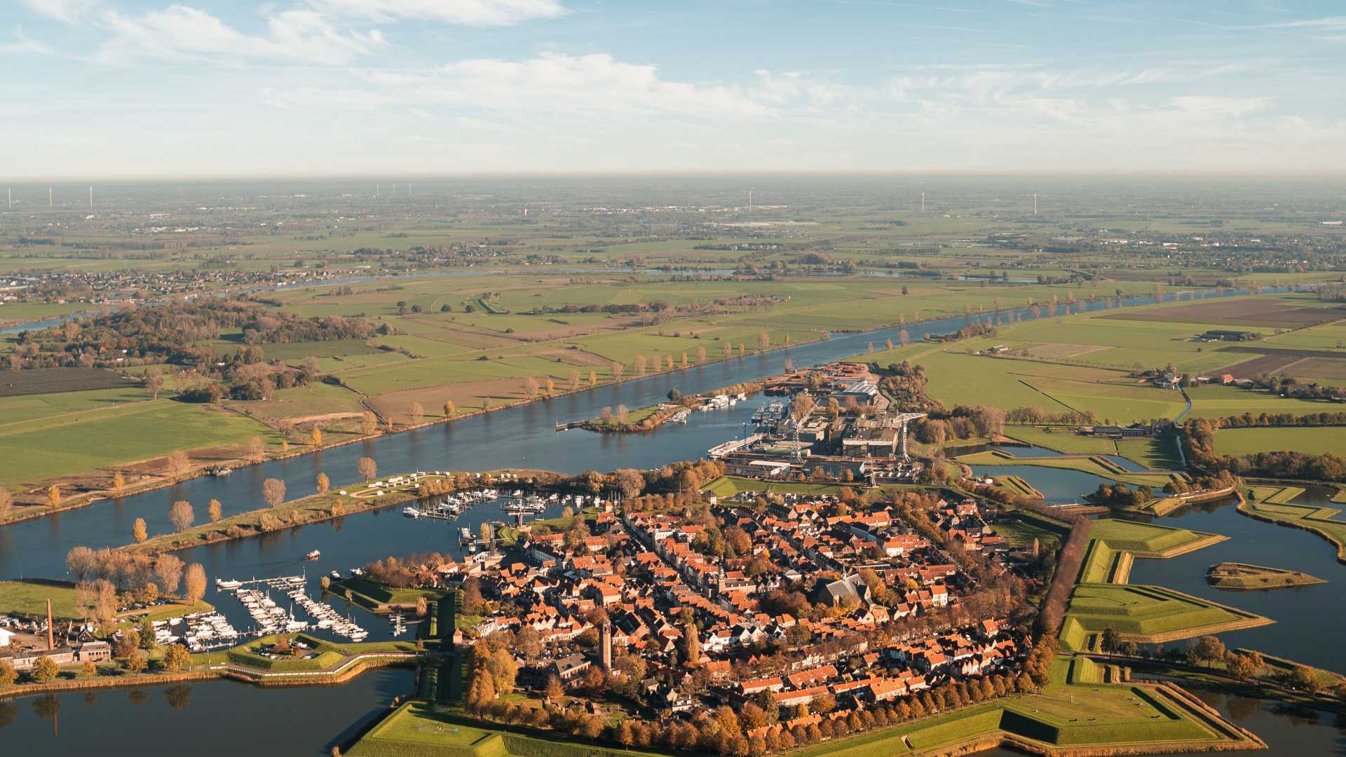 Luftaufnahme von Heusden, Niederlande, mit einem sich durch gepflügte Felder schlängelnden Fluss und einer charmanten Stadt.