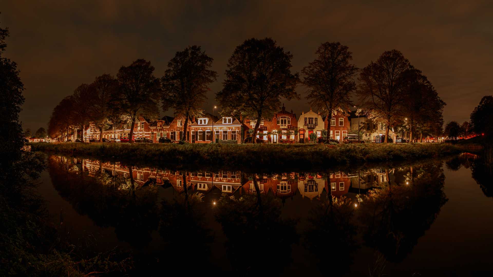 Charmante Middelburgse huizen en bomen weerspiegeld in een gracht onder de nachtelijke hemel.