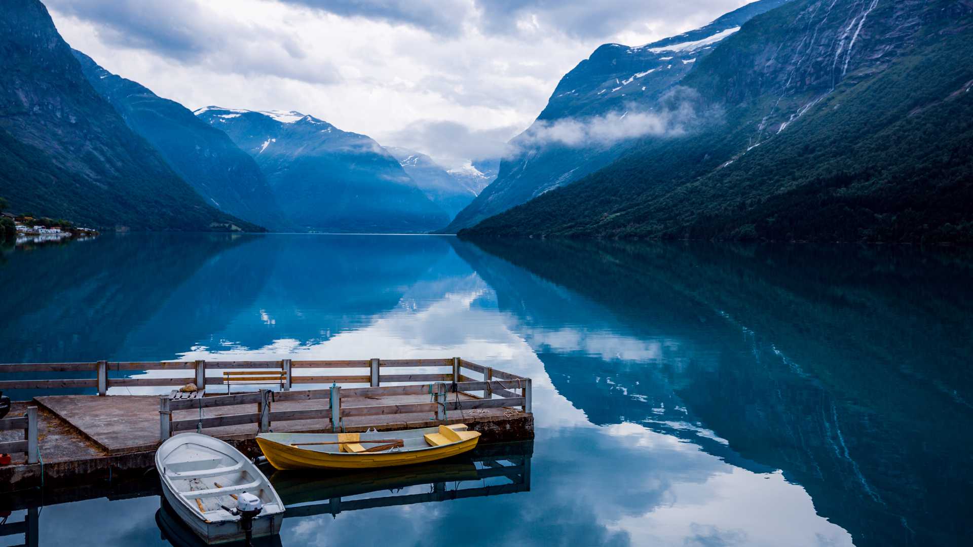 Ruhiger Lovatnet-See in Norwegen mit angedockten Booten, umgeben von hoch aufragenden Bergen und ruhigen Spiegelungen.