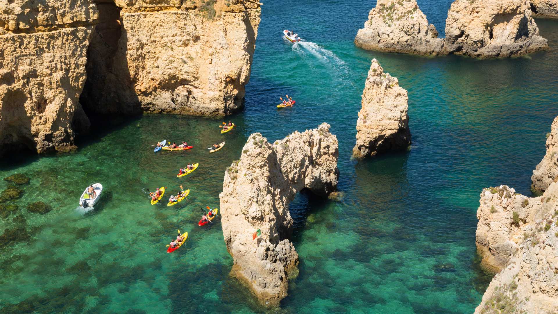 Kleurrijke kajaks varen door het turquoise water en de rotsachtige kliffen van Lagos, Portugal.