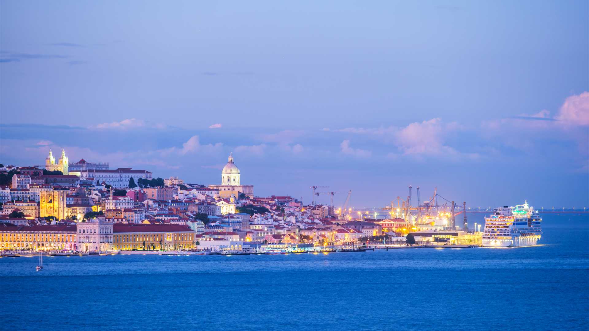 Lisbon cityscape at twilight, viewed across the Tagus River.