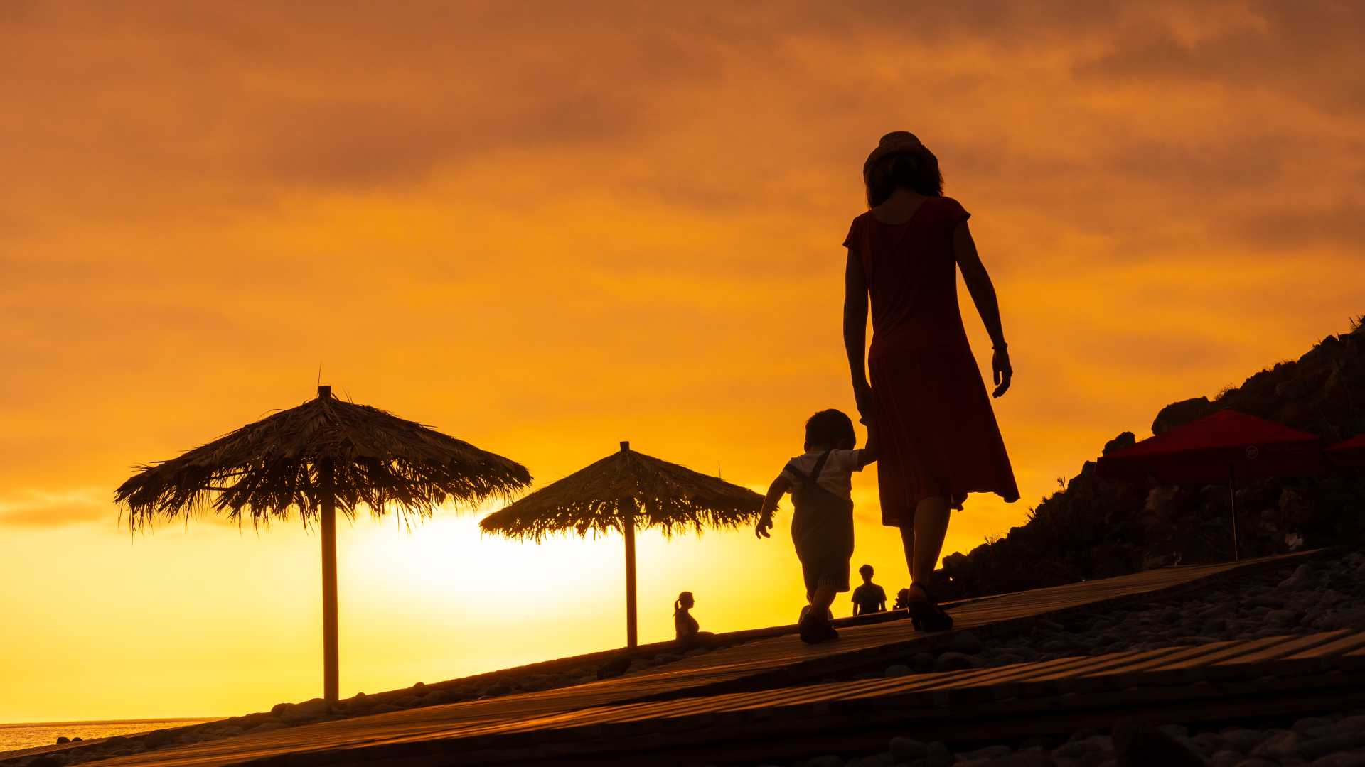 A silhouetted mother and child walking on a beach at sunset in Ponta do Sol, Madeira.