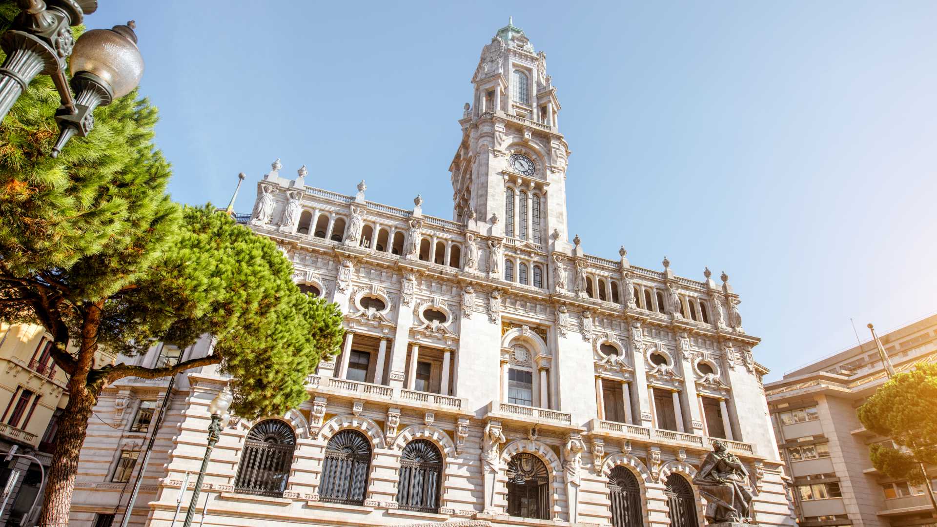 The ornate facade of Porto City Hall under a clear blue sky, framed by lush green trees.