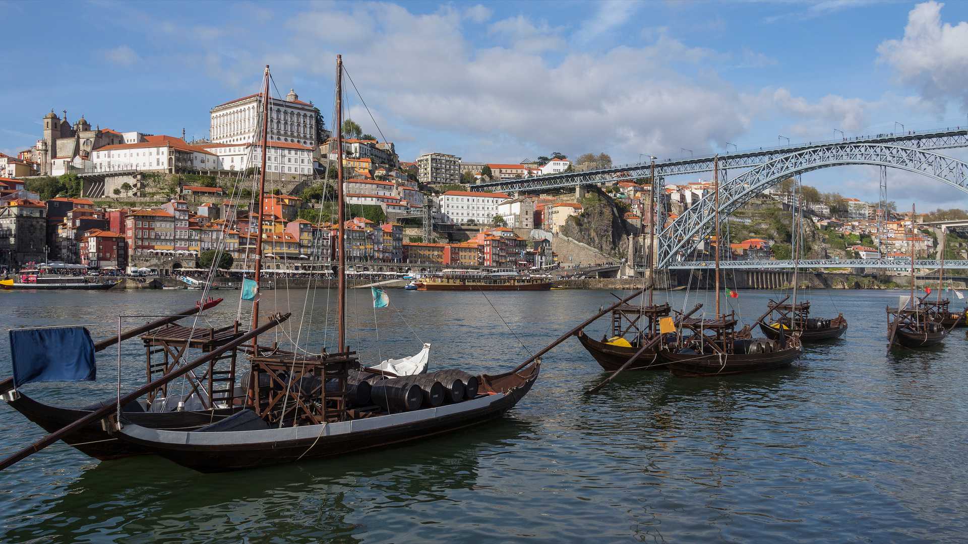 Traditional boats on the Douro River, set against the backdrop of Porto's historic buildings and the Dom Luís I Bridge.