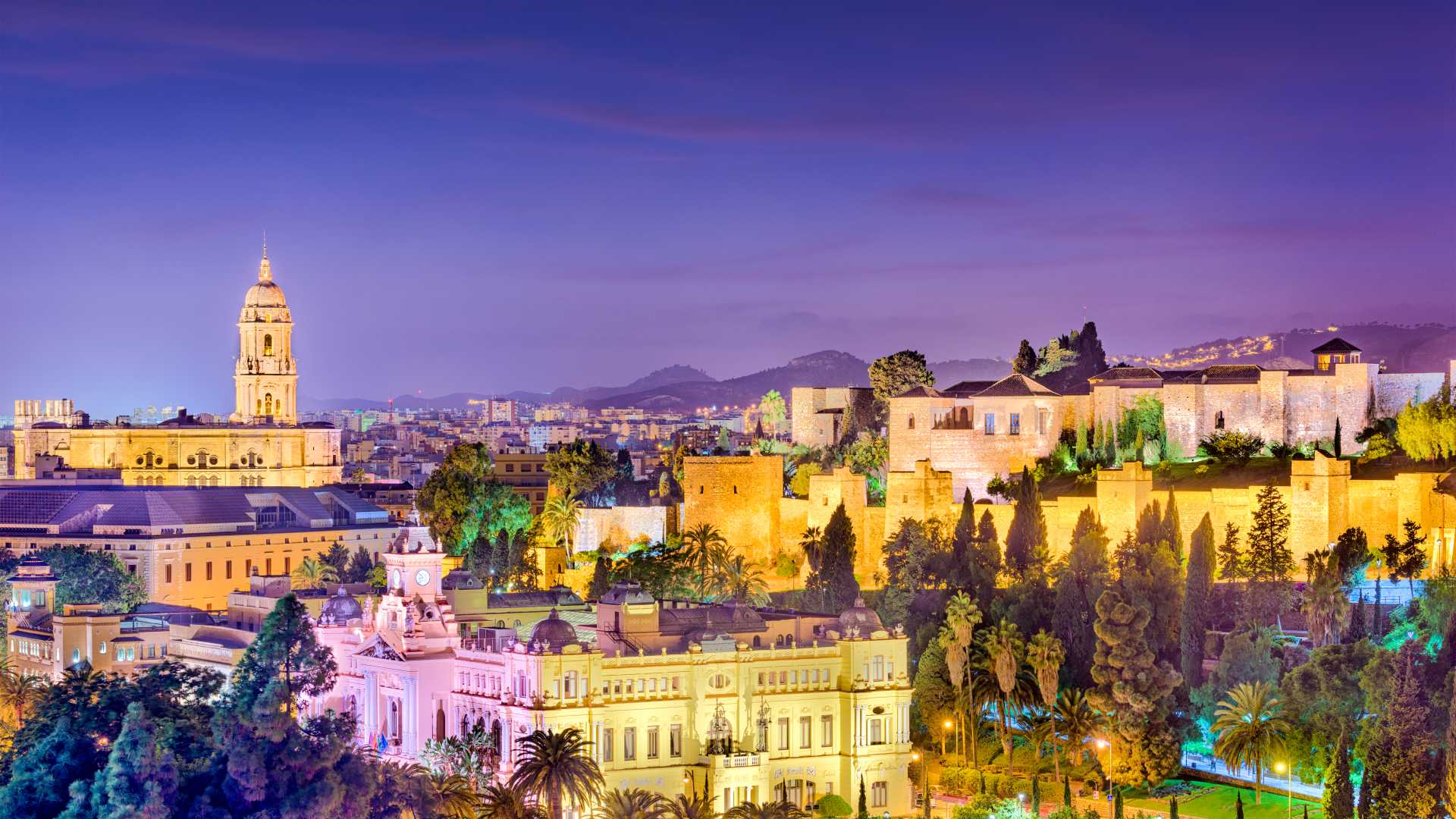 Die Skyline der Altstadt von Málaga in der Abenddämmerung mit der beleuchteten Kathedrale und der historischen Festung Alcazaba.