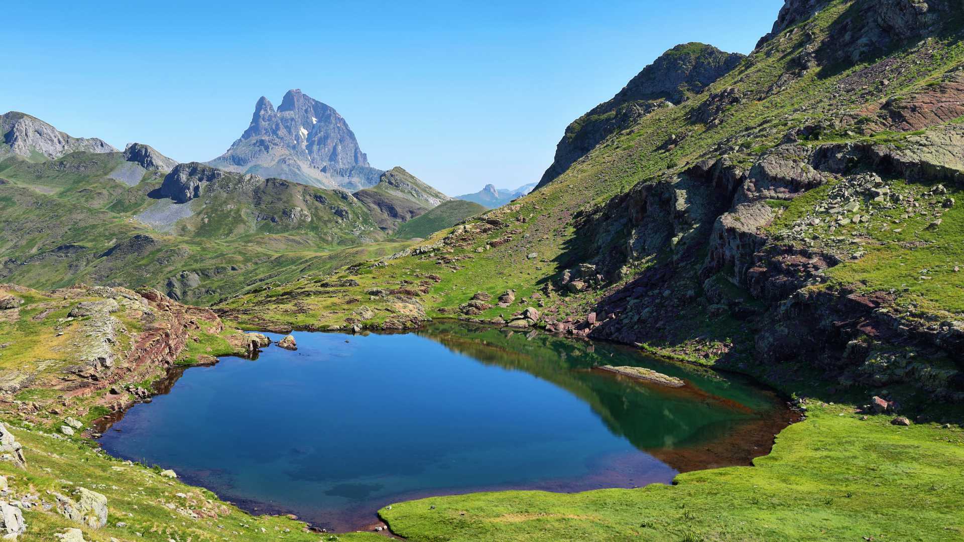 Stunning view of Pic du Midi d'Ossau from Anayet plateau, with a serene lake reflecting the mountain.