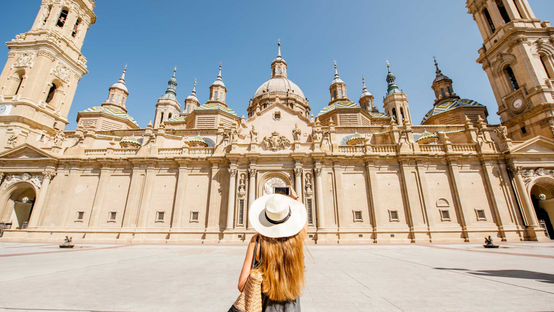 Eine Frau mit Sonnenhut steht an einem sonnigen Tag vor der majestätischen Basilika del Pilar in Zaragoza.