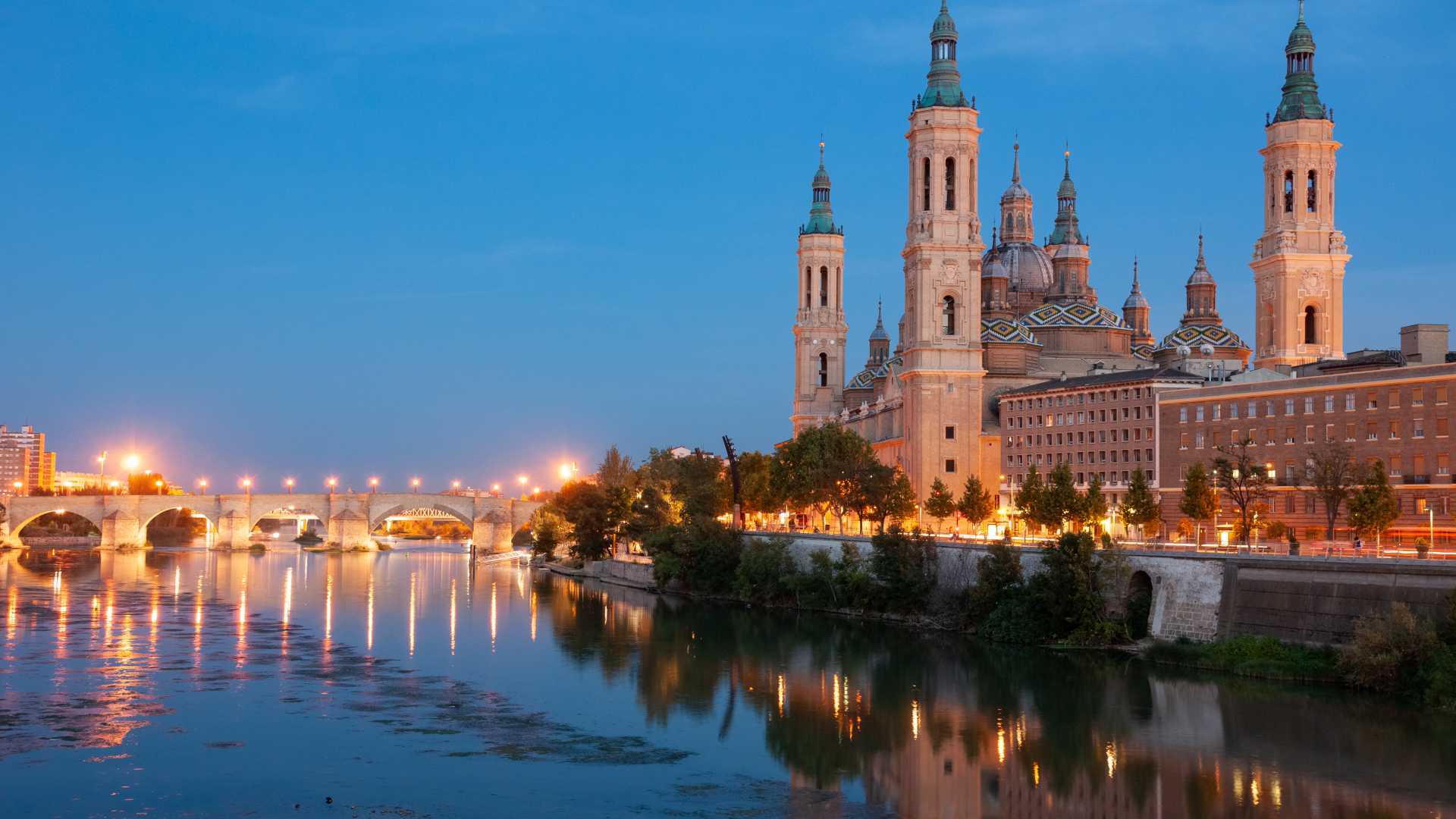 The Basilica of Our Lady of the Pillar illuminated at dusk, reflecting in the Ebro River in Zaragoza, Spain.