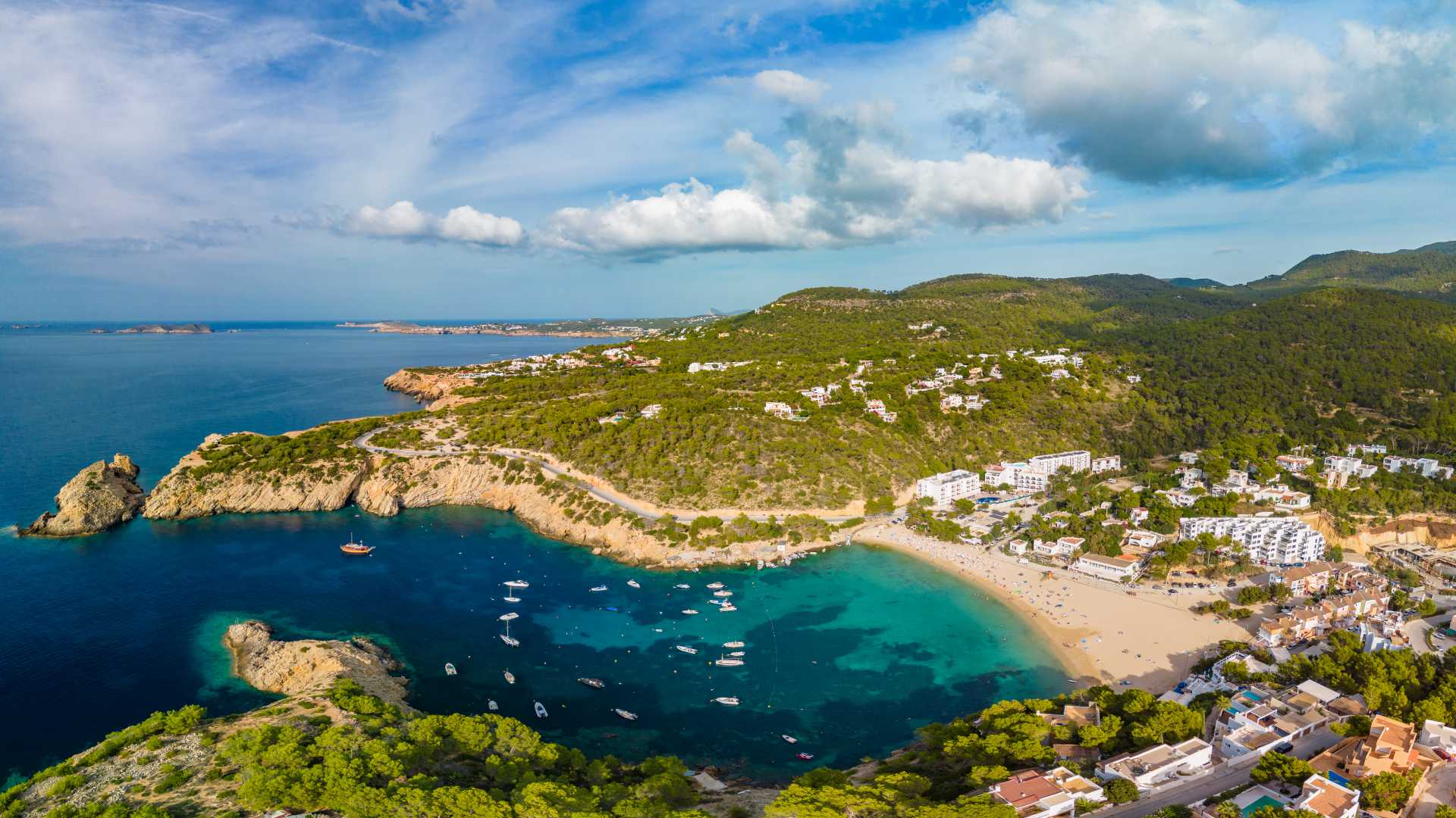 Vue aérienne des eaux turquoise, de la plage de sable et des collines verdoyantes de Cala Vadella, sur l'île d'Ibiza, en Espagne.