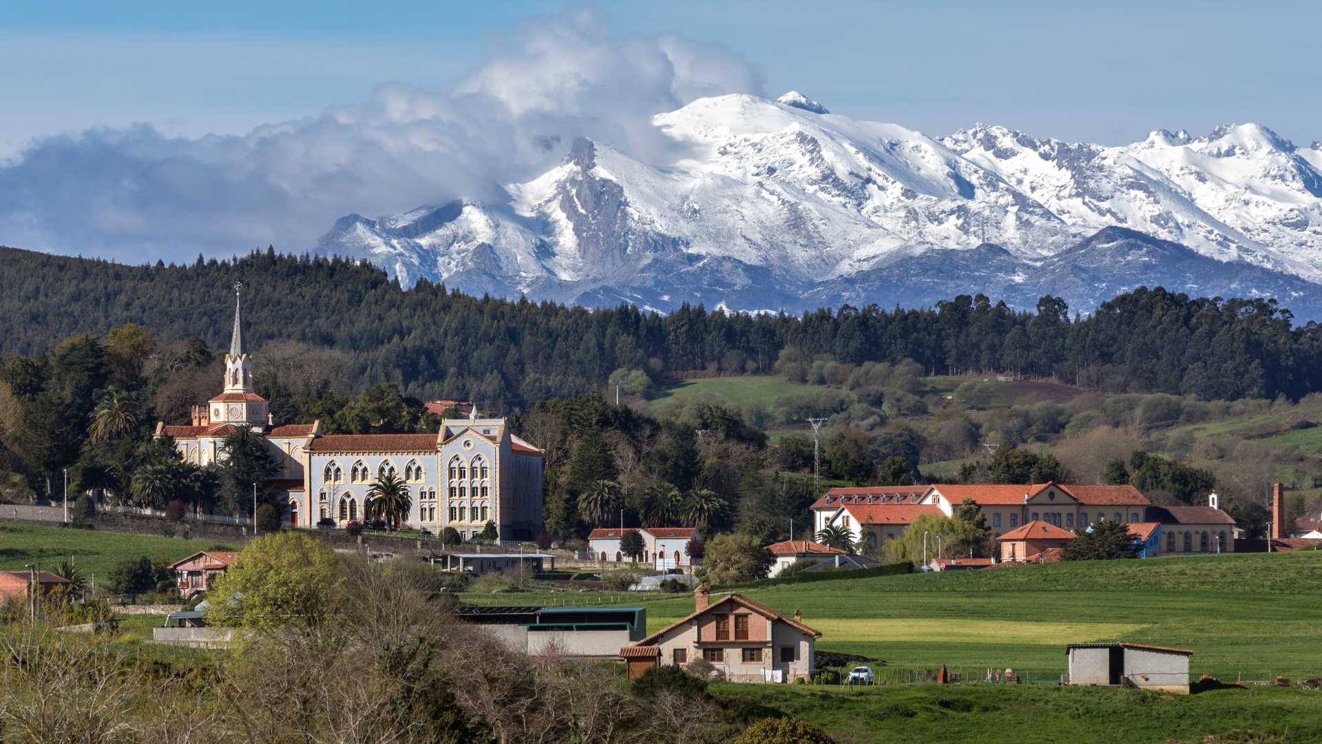 Die schneebedeckten Berge erheben sich hinter der charmanten Stadt Corbreces, eingebettet in die üppige grüne Landschaft Kantabriens.