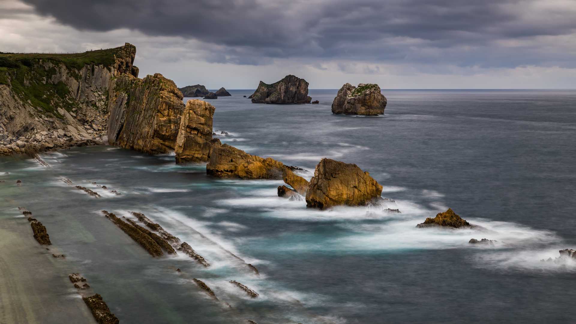 Dramatic cliffs and rock formations at Playa de la Arnia, Cantabria, under a moody, cloudy sky.