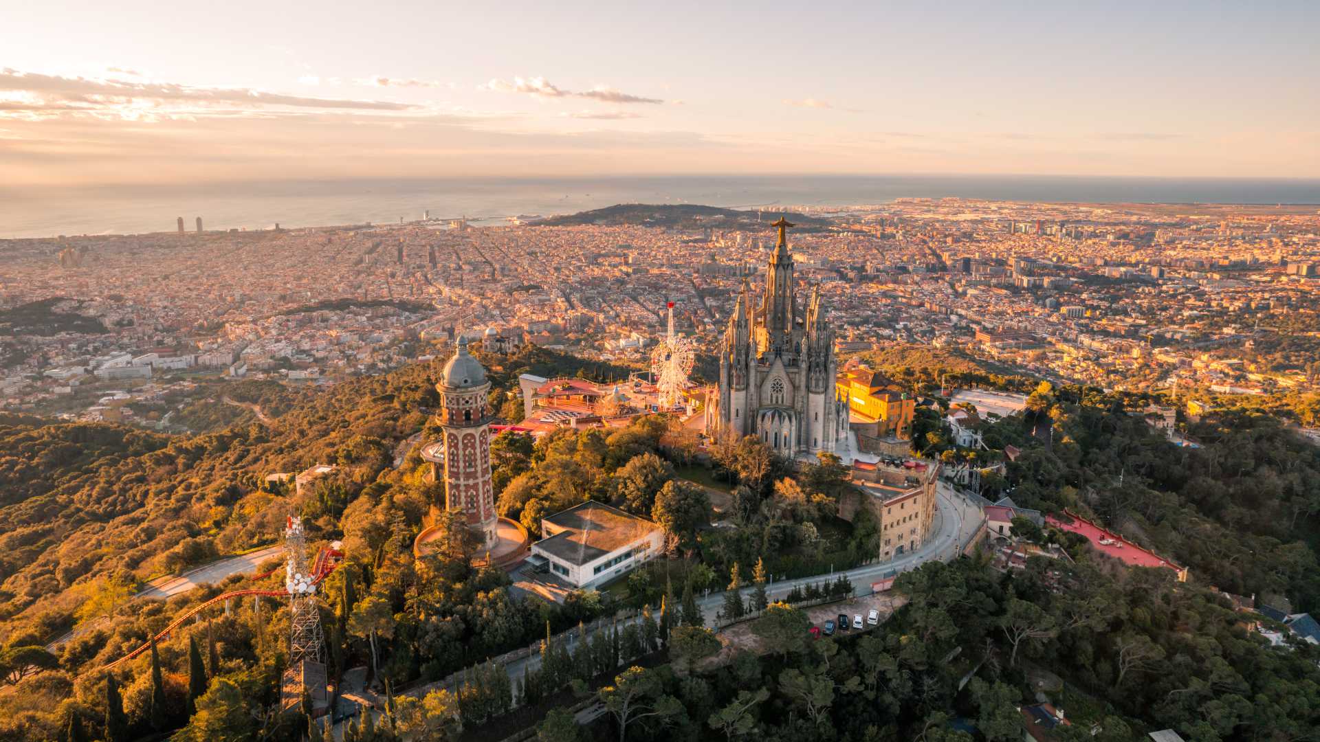 Sunrise over Barcelona skyline with Sagrat Cor temple atop Tibidabo mountain, bathed in golden light.