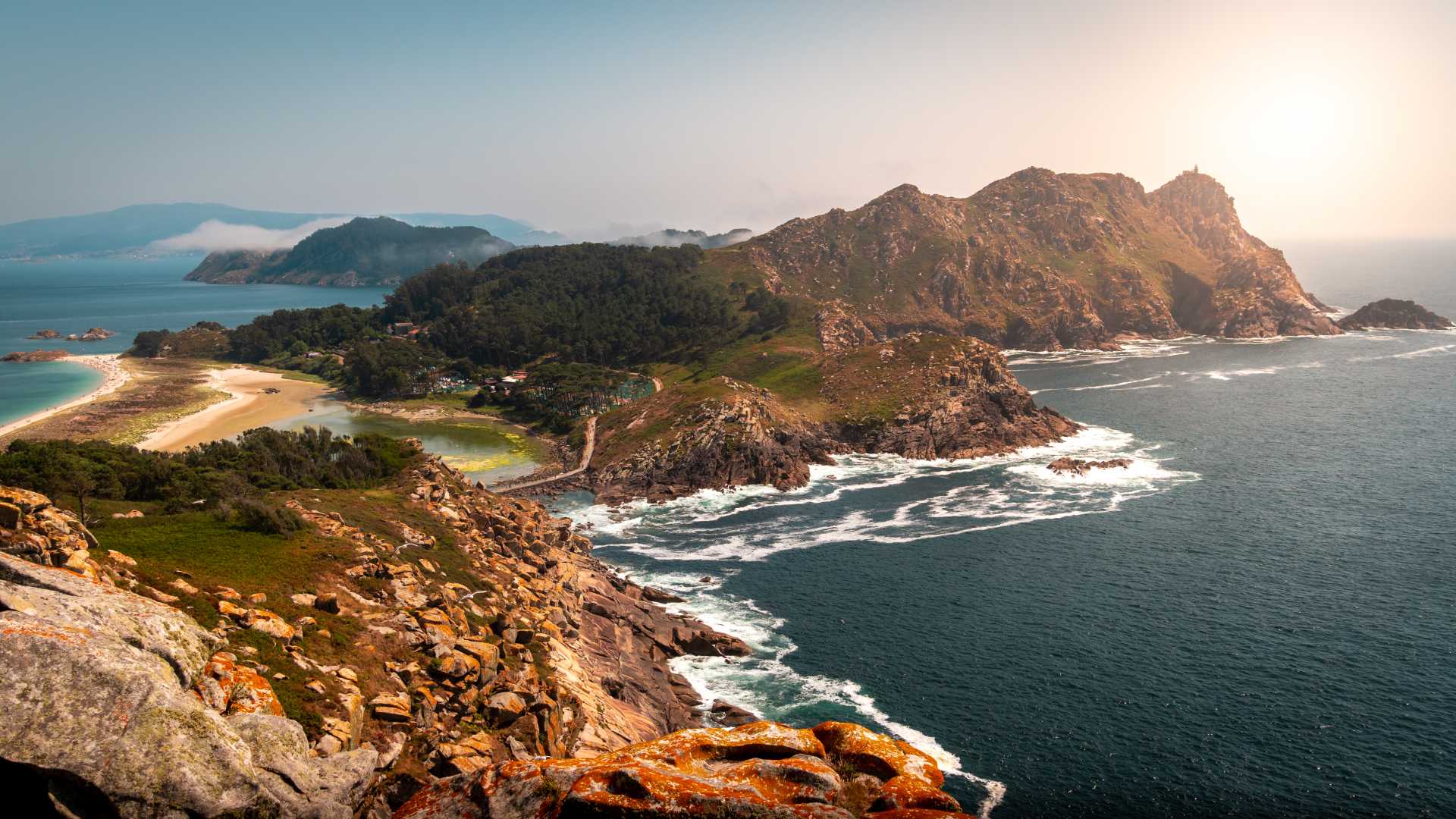 Rugged coastline of the Cies Islands, Spain, with azure waters and lush greenery under the sun.