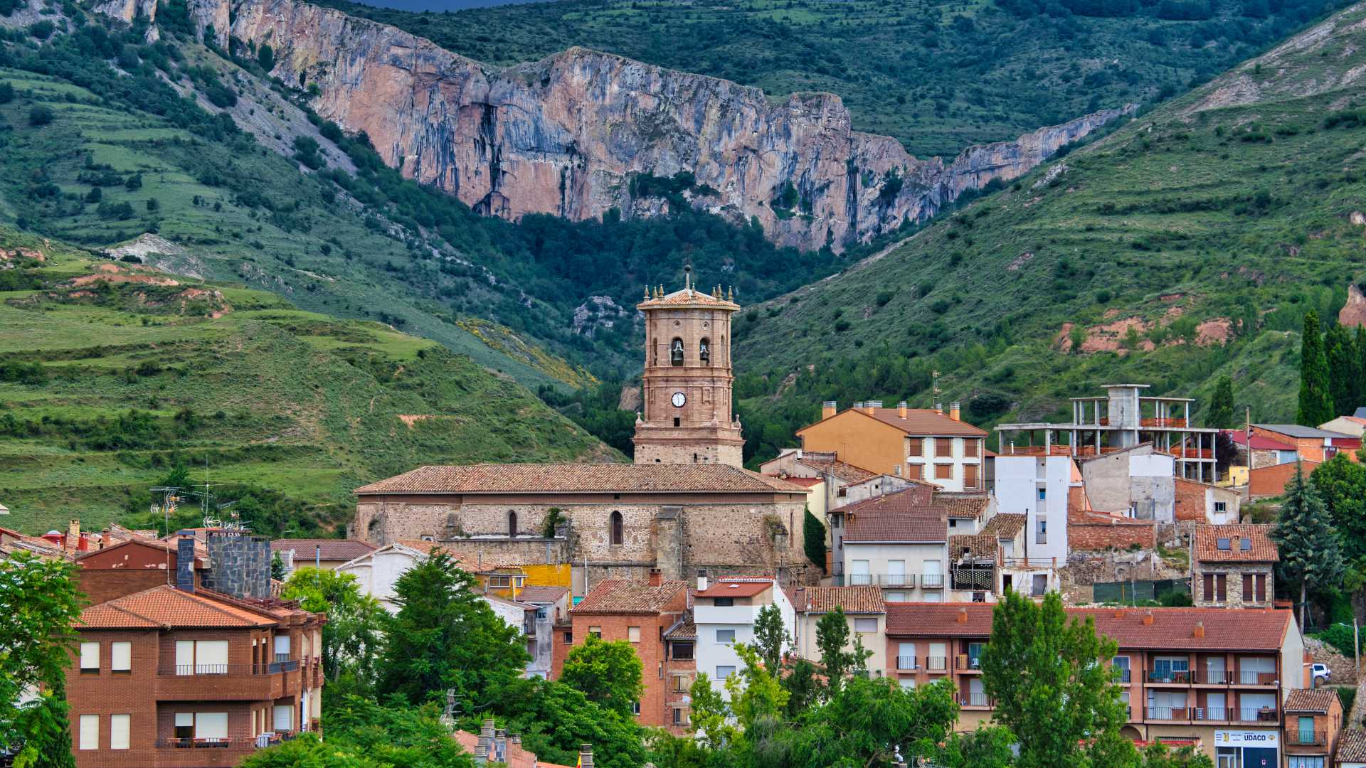 Medieval cathedral in Viguera, Spain, surrounded by colorful houses and lush green mountains.