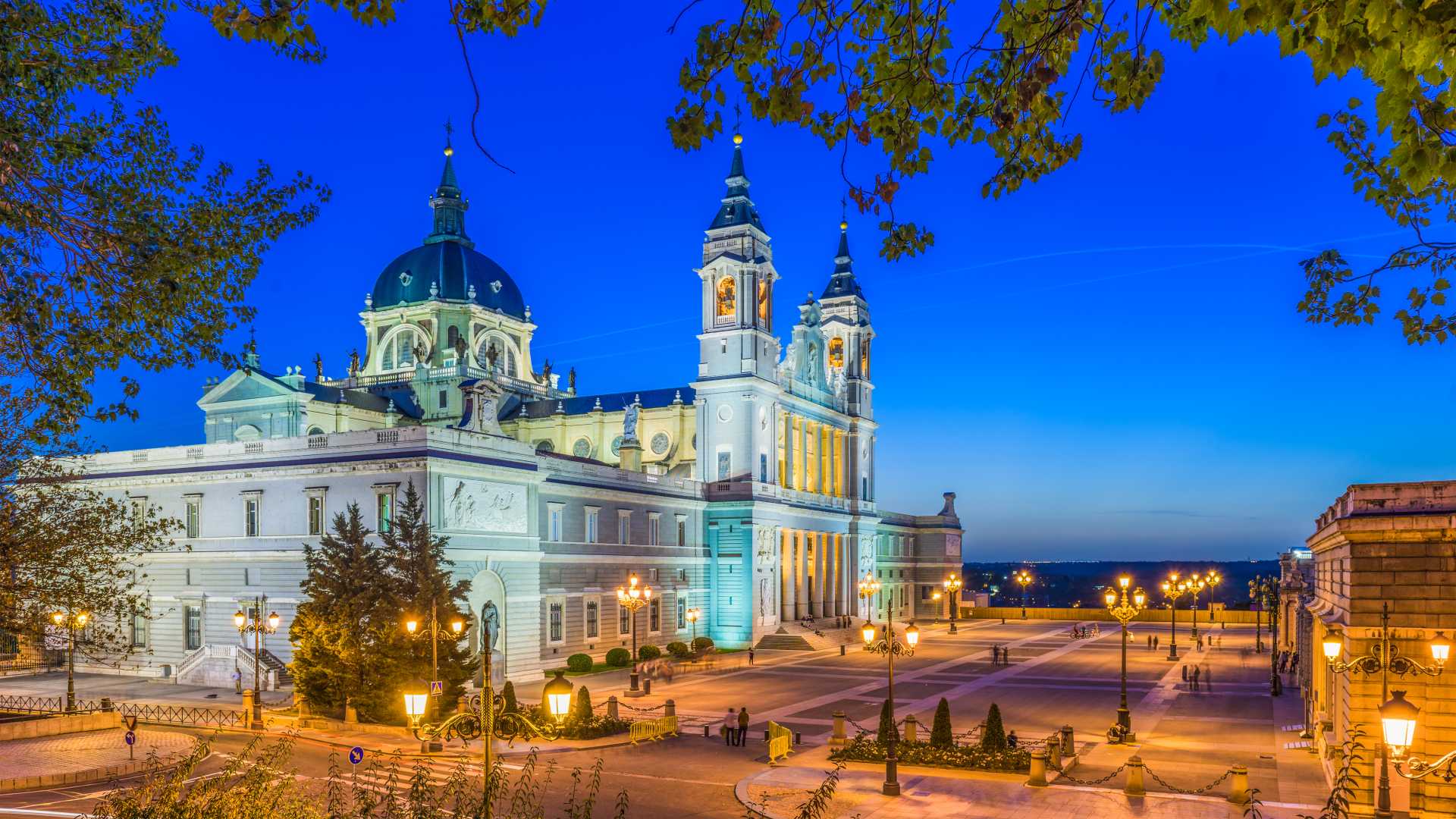 Almudena Cathedral in Madrid illuminated at dusk, with a vibrant blue sky and ornate architecture.